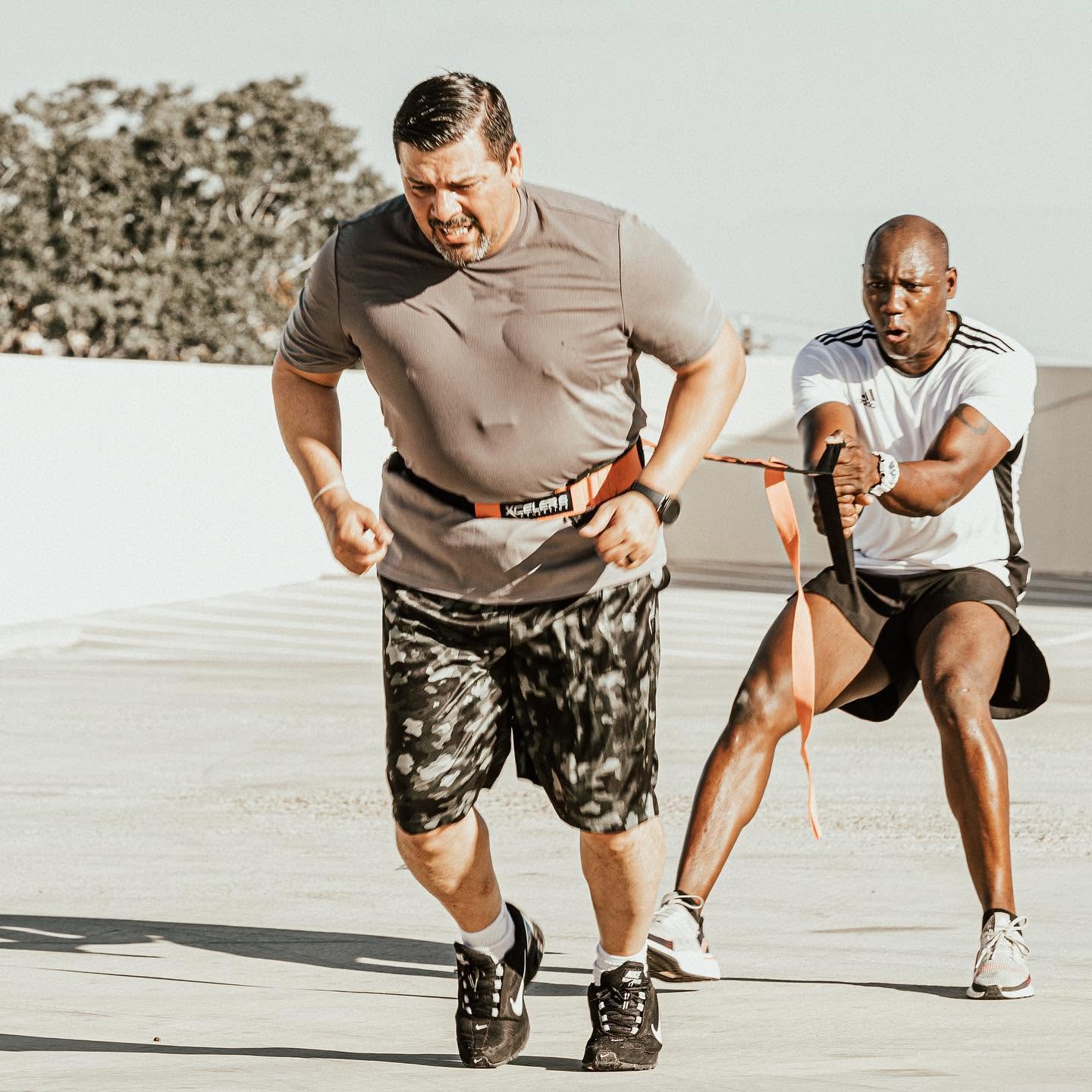 A client powering through a resistance-harness sprint with Alex Ampadu anchoring behind — the kind of coaching Harlingen clients drive to Brownsville for