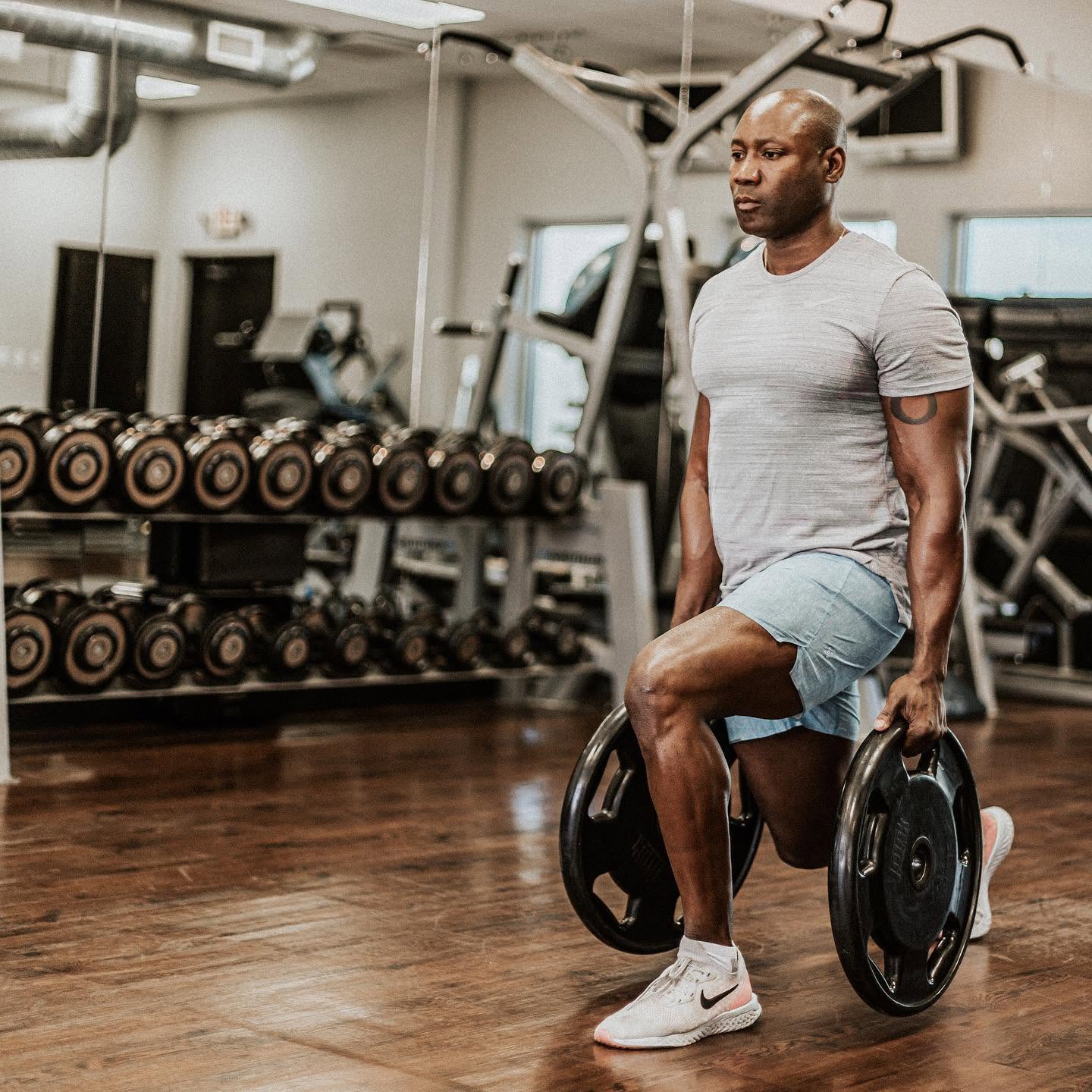 Alex 'Mr. 101' Ampadu doing walking lunges with weight plates during a one-on-one session at his private studio in Brownsville, TX