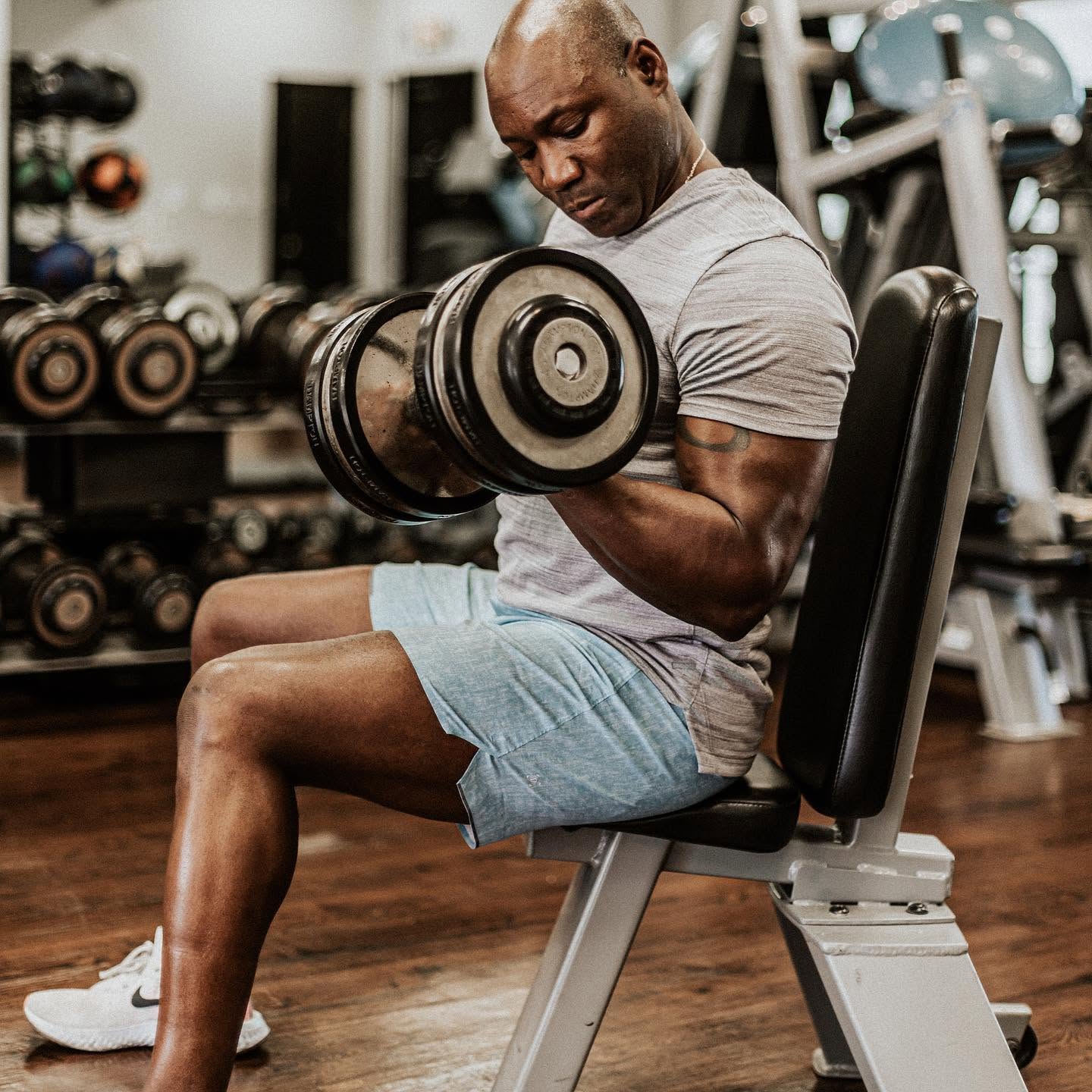 Alex Ampadu doing seated dumbbell curls — muscle-building work with free weights at 101 Fitness in Brownsville, TX