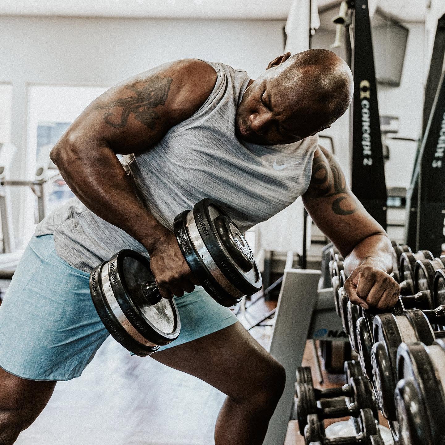 Alex Ampadu rowing a heavy dumbbell at the rack of his private 101 Fitness studio in Brownsville — every session programmed one-on-one