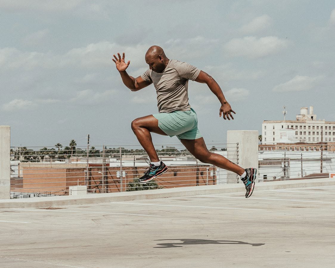 Alex 'Mr. 101' Ampadu in a full sprint leap above a Brownsville rooftop — energy that travels with your online program