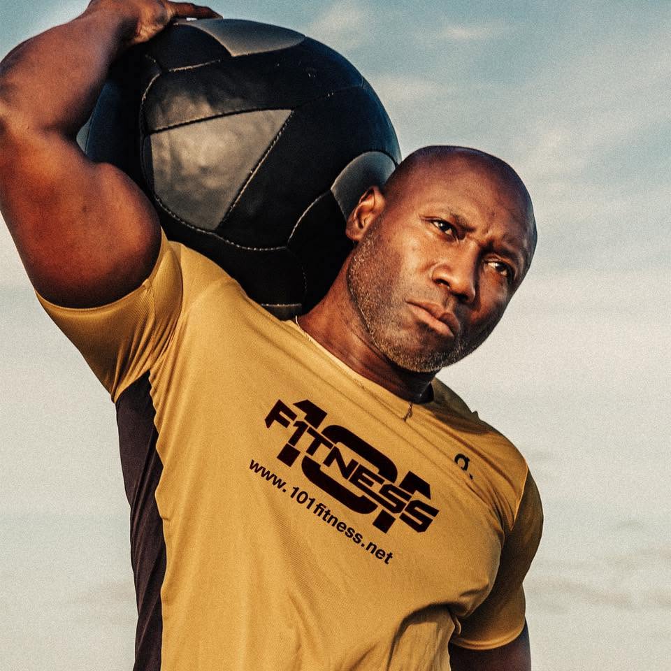 Alex 'Mr. 101' Ampadu, NASM certified personal trainer at 101 Fitness in Brownsville, shouldering a medicine ball